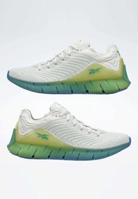 Baskets de sport avec une tige en mesh blanc, une semelle translucide verte et jaune, des accents texturés et une semelle extérieure en caoutchouc bleu.