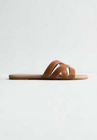 Bruna slidesandaler av konstläder med crisscross-remmar, platt gummisulor och sömnad detaljer för extra textur.
