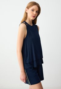 Marineblauwe mouwloze top met gelaagd ontwerp, voorzien van een ronde halslijn en smalle straps. Gecombineerd met bijpassende shorts en zijstrepen.