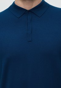 Homme portant un polo bleu foncé boutonné avec un col plié, visible des épaules jusqu'à la poitrine.