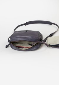 Borsa a tracolla in pelle di colore viola scuro, con un compartimento principale con zip e una fodera a righe, oltre a una pochette staccabile. Include una tracolla regolabile.