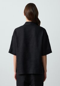 Camicia nera in lino a maniche corte con una vestibilità rilassata, dotata di colletto e spacchi laterali all'orlo per facilitare i movimenti.