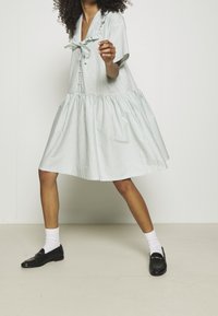 Robe en coton rayée avec des manches courtes, col volanté et jupe évasée. Associée à des mocassins noirs et des chaussettes blanches.