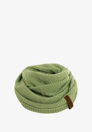 Lichtgroene gebreide beanie en bijpassende sjaal, gedragen door een persoon met golvend haar. De materialen hebben een gestructureerde, gezellige uitstraling.