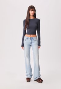 Dolgimi rokavi, skrajšan mornarsko moder top, v kombinaciji s svetlo modrimi širokimi jeans hlačami. Model nosi masivne rjave platformske sandale z zlatimi žebljički.