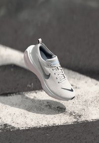 Athletic shoe in white with grey accents, featuring a textured upper, a rounded sole, and a cushioned heel. Nike logo displayed prominently.