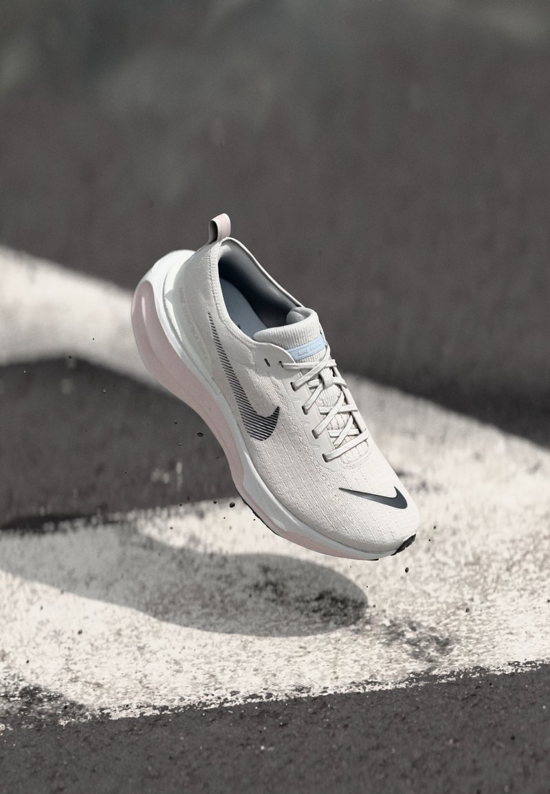 Zapatilla deportiva en blanco con acentos en gris, que presenta una parte superior texturizada, una suela redondeada y un talón amortiguado. Logo de Nike exhibido de manera prominente.