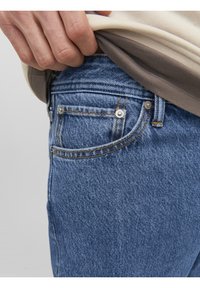 Blå denimjeans har en klassisk design med fem fickor, kontrasterande gula sömmar och metallknappar nära midjan.