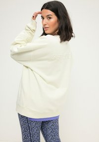 Sudadera oversized de color crema con texto en relieve "GET STR8", combinada con leggings ajustados de leopardo azul. Tejido suave, corte relajado.