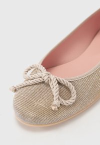 Bailarinas con un upper de tela dorada texturizada, con punta redonda, plantilla suave en rosa y un lazo decorativo de cuerda en la parte frontal.