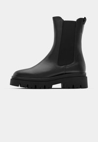 Svart Chelsea-støvel i skinn med tykk såle med knotter, elastiske sidepaneler og trekkflapp bak, vist i profil på hvit bakgrunn.