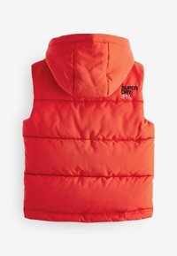 Gilet rembourré rouge avec capuche, présentant des coutures horizontales et un logo brodé noir "SUPER DRY JPN." Texture de tissu lisse et design ajusté.