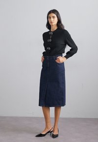 Melnas, ribotas garo piedurkņu blouse ar trim dekoratīvām pogām; tumši džinsa midi svārki ar priekšējo šķēlumu; melnas norādītās kurpes.