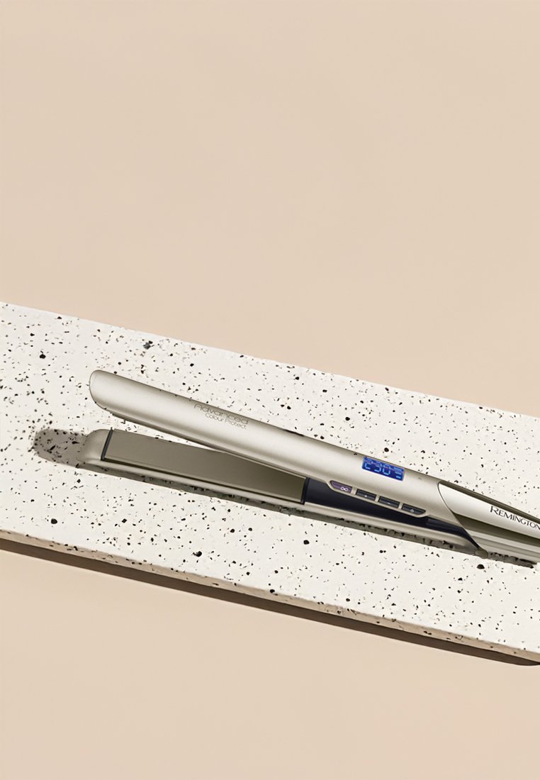 Piastra per capelli argentata con display digitale e pulsanti di controllo, adagiata su una superficie bianca maculata. Presenta un design elegante e raffinato.