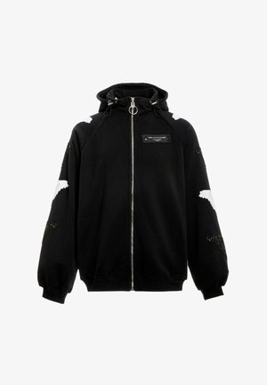 Sudadera con capucha negra con cremallera, tirador de cremallera con anillo grande, parches de alas blancas y negras en las mangas y los hombros, y una etiqueta negra en el pecho.