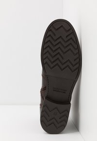 Zapato de cuero marrón con una suela de goma texturizada que presenta un patrón de zigzag. Las marcas incluyen "JACK & JONES" y la talla "43."