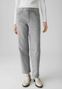 Jeans in denim grigio chiaro con vestibilità dritta, cinque tasche e dettagli di cucitura visibili. Indossati con mocassini beige.