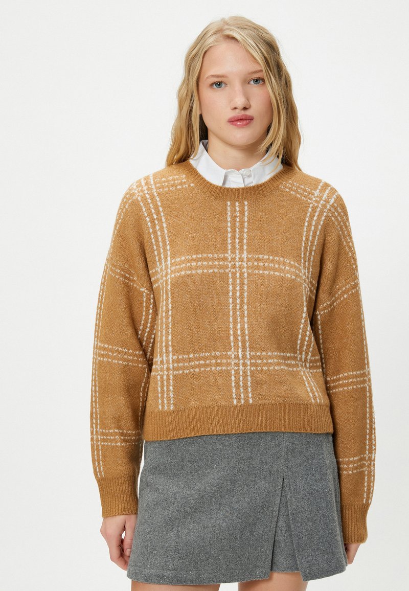 Senfgelbes gestricktes Sweater mit weißem Karomuster, rundem Halsausschnitt und gerippten Bündchen. Kombiniert mit einem grauen plissierten Minirock.
