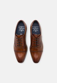 Chaussures habillées en cuir marron avec une texture lisse, un bout pointu et des lacets noirs. Présente des coutures discrètes et un logo sur la semelle intérieure.
