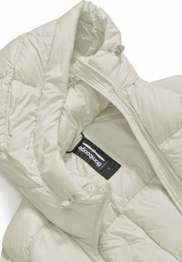 Giacca a vento imbottita in beige chiaro, con texture liscia, chiusura con zip ed etichetta interna. Include un colletto alto e dettagli con cordoncino.