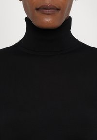 Zwarte geribbelde coltrui met een aansluitend ontwerp. Glad textuur, hoge kraag en geen zichtbare patronen of hardwareaccenten.