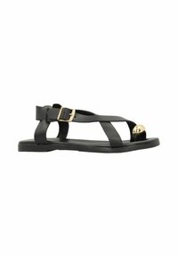 Black leather sandal features a flat sole, cross straps, a buckle closure, and a prominent golden round accent at the toe.
