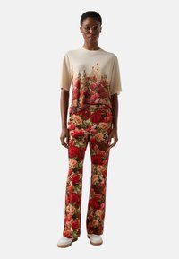 Floral-print top in cream and red hues, paired with matching floral trousers. Both made of soft fabric with a relaxed fit and wide legs.