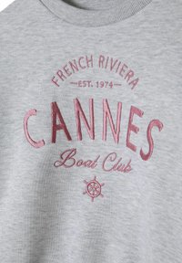 Szürke kapucnis pulóver bordázott nyakkivágással, rózsaszín hímzéssel, amelyen a "CANNES Boat Club" és a "FRENCH RIVIERA EST. 1974" felirat látható.