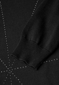 Svart stickad tröjsleeve med manschett, som pryds av silverfärgade rhinestones i ett stjärnformigt mönster på tyget.