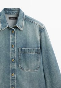 Světle modrá džínová košile s hnědými knoflíky, jednou náprsní kapsou a klasickým límcem, označená Massimo Dutti.