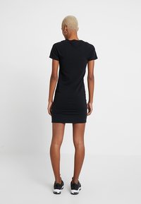 Svart bomulls t-shirtklänning med en figurnära silhuett, korta ärmar och rund halsringning. Dekorerad med rynkor vid midjan, kombinerad med sneakers.