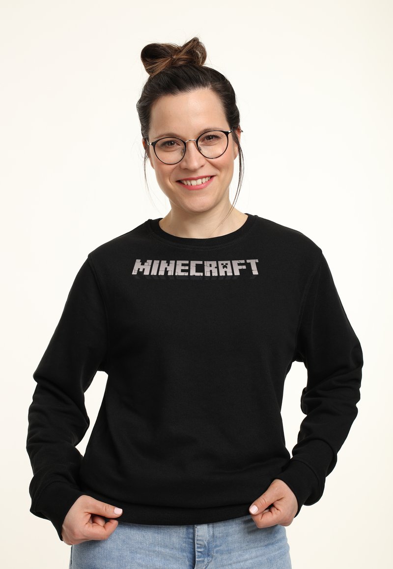 Felpa nera in misto cotone, con un logo "MINECRAFT" in caratteri squadrati di grandi dimensioni sul petto. Design semplice con collo rotondo.
