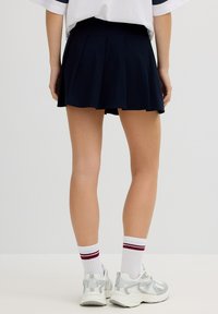 Falda plisada de color azul marino con una cintura ajustada, con una textura suave. Zapatillas deportivas plateadas y calcetines blancos con franjas color burdeos completan el atuendo.