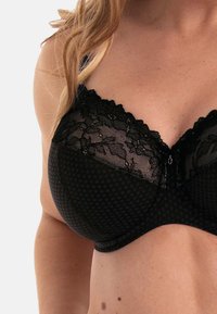Zwarte kant beha met stippenmesh en bloemenaccenten, met beugelsupport en verstelbare bandjes. Aandacht voor detail in textuur van de stof.