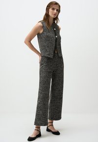 Schwarze und weiße Tweed-Weste, cropped, mit zwei runden Knöpfen, kombiniert mit passenden weit geschnittenen Hosen. Verfügt über ein strukturiertes Muster.