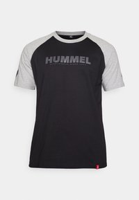 Svart T-skjorte med kontrastgrå raglanermer, med en stor "HUMMEL"-logo i grått på forsiden. Mykt stoff med rund hals.