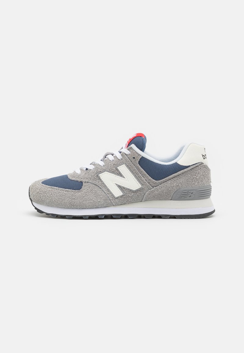 Zapatillas de ante gris y malla con acentos blancos, detalles azules y una etiqueta roja en la lengüeta. Cuenta con una suela de goma con diseño de dibujo.