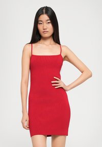 Abito mini rosso a coste con spalline sottili e scollatura quadrata, forma aderente e texture liscia.