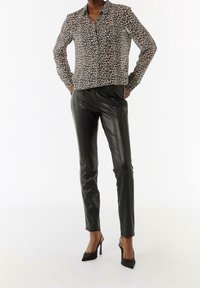 Chemise à boutons imprimé léopard avec col, associée à un pantalon en cuir noir coupe slim et des chaussures à talons hauts noires.