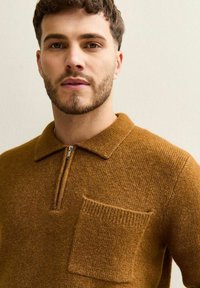 Bruine half-zip trui van gestructureerd breimateriaal met een klein borstzakje en een klassieke kraag.