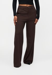 Καφέ τζιν προσαρμοσμένης εφαρμογής με ίσια γραμμή, κατασκευασμένοι από λείο ύφασμα. Διαθέτουν κλείσιμο με κουμπί και πλαϊνές τσέπες.