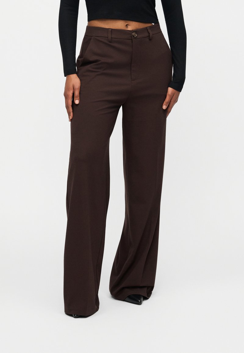 Καφέ τζιν προσαρμοσμένης εφαρμογής με ίσια γραμμή, κατασκευασμένοι από λείο ύφασμα. Διαθέτουν κλείσιμο με κουμπί και πλαϊνές τσέπες.