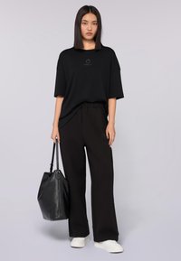 Svart oversized t-shirt med rund halsringning och logotyp framtill, kombinerad med högmidjade svarta byxor och en strukturerad svart handväska.