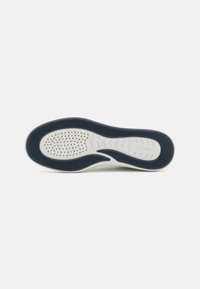 Semelle de chaussure en caoutchouc blanc texturé, avec un motif ondulé bleu marine et des perforations pour la respirabilité.