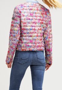 Vadderad, flerfärgad jacka med blommönster, med rund krage och elastiska manschetter, ihop med åtsittande blå jeans.