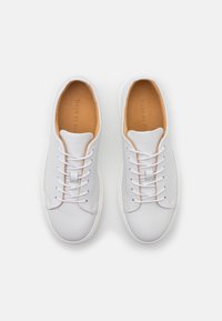 Sneaker bianchi in pelle con una superficie liscia, punta tonda e interno beige a contrasto. Presentano una chiusura con lacci standard e un design minimalista.
