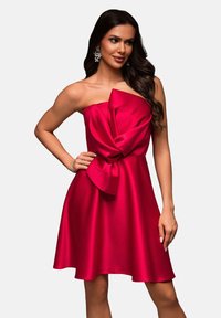 Robe sans bretelles, longueur genou, en satin rouge vif avec un grand nœud à la taille, présentant une texture lisse et brillante et une jupe évasée.