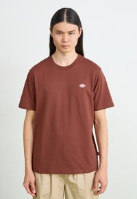 Bruine katoenen T-shirt met ronde hals, korte mouwen en een klein logo op de borst. Soepele textuur, relaxte pasvorm.