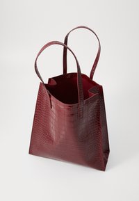 Sac fourre-tout bordeaux en simili cuir brillant avec une texture crocodile, doté de deux poignées robustes et d'un dessus ouvert.