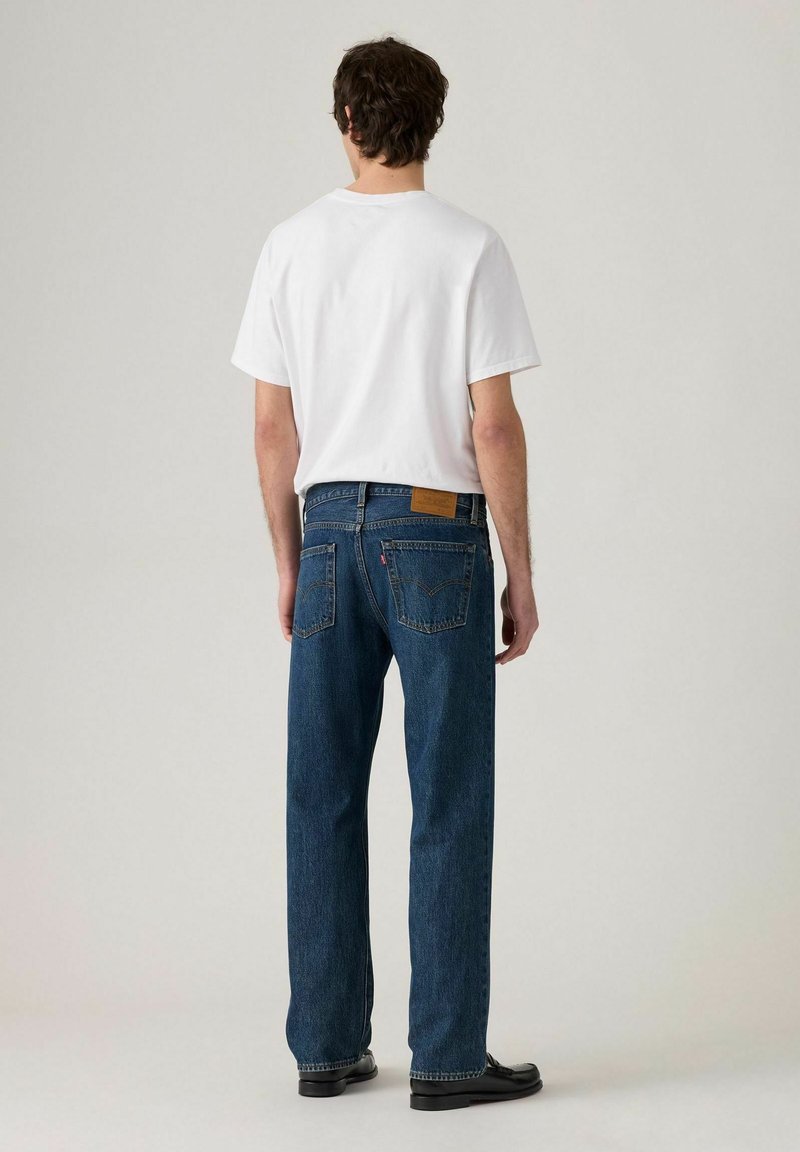 Witte T-shirt met ronde hals, gecombineerd met loszittende blauwe spijkerbroek. De jeans hebben een leren label en twee achterzakken.